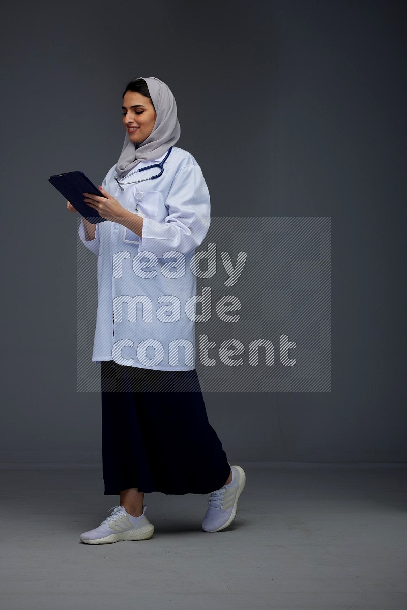 A Saudi doctor wearing a light gray head scarf standing and crossing her hands eye level on a grey background