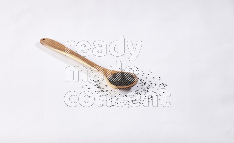 A wooden ladle full of black seeds on a white flooring
