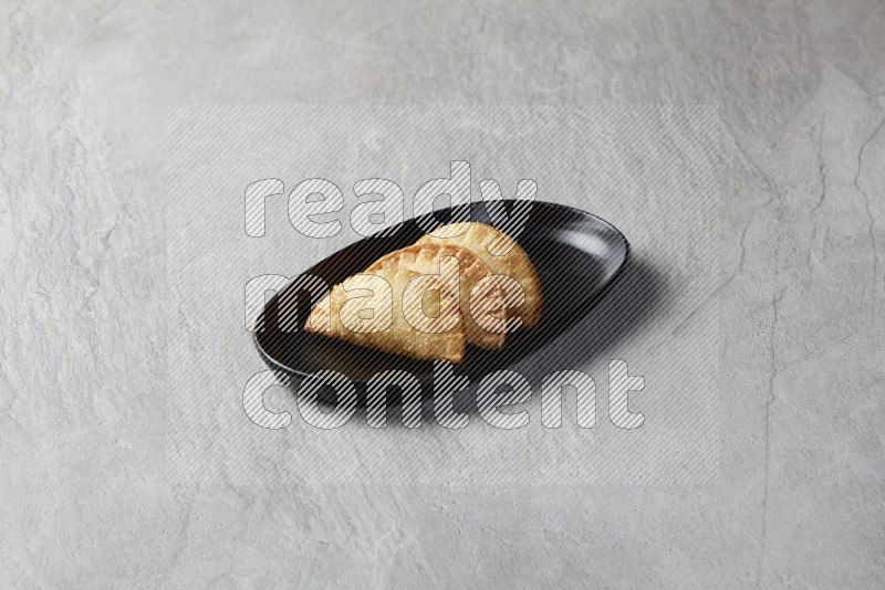Three fried sambosas in an oval shaped black plate on a gray background