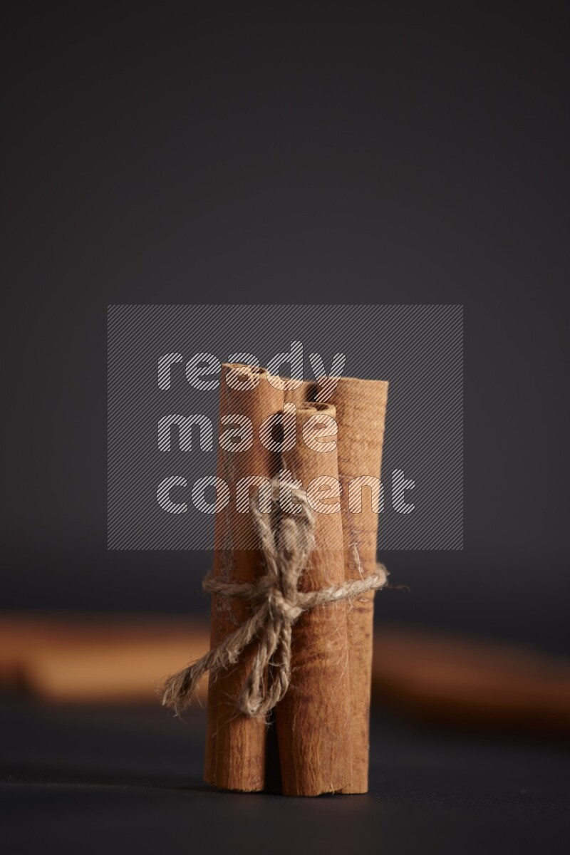 4 Cinnamon sticks stacked and bounded with more sticks in the background on black flooring