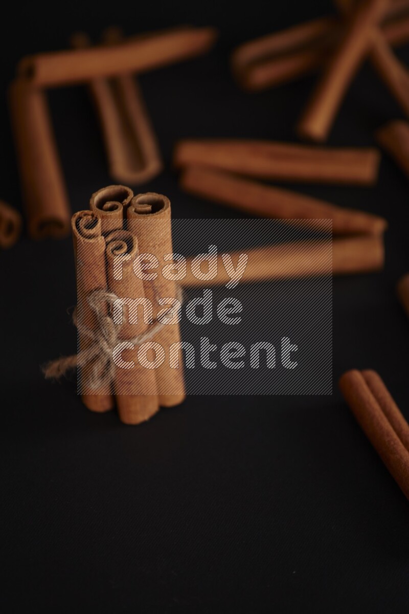 4 Cinnamon sticks stacked and bounded with more sticks in the background on black flooring