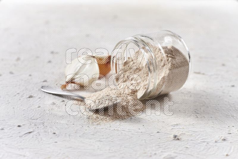 A glass jar full of onion powder flipped with some spilling powder on white background