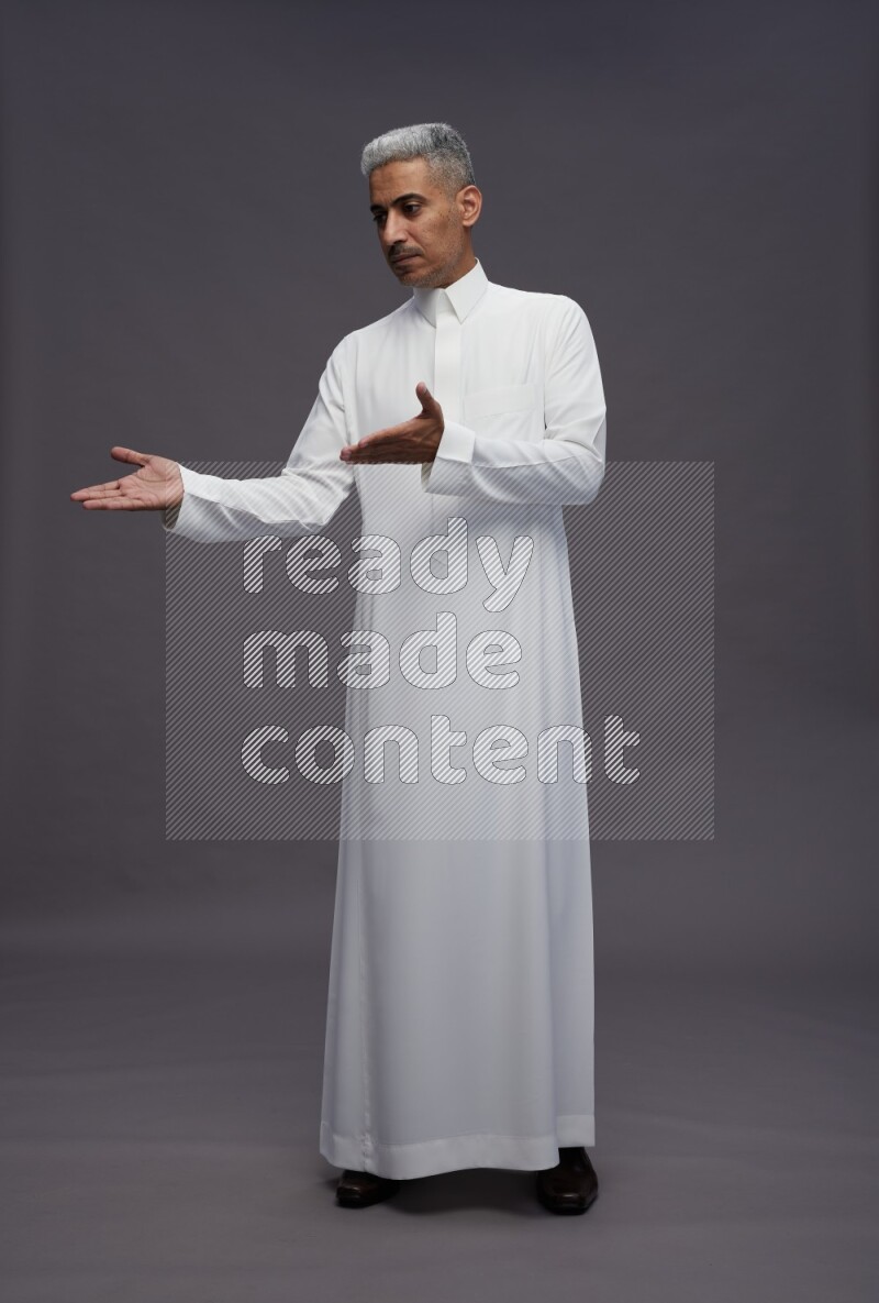 Saudi man wearing thob standing interacting with the camera on gray background