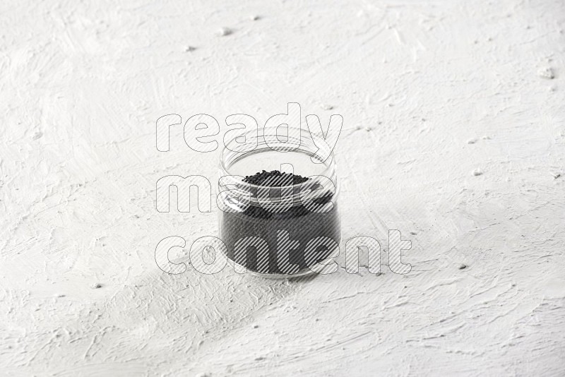 A glass jar full of black seeds on a textured white flooring