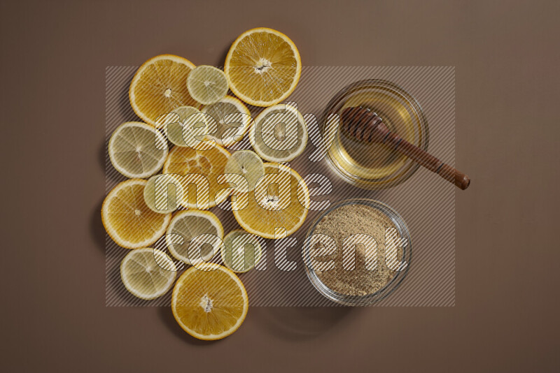 Two bowls full of honey and ground ginger with some of citrus fruits such as lemon and orange on a beige background