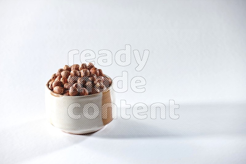 A beige ceramic bowl full of peeled hazelnuts on a white background in different angles
