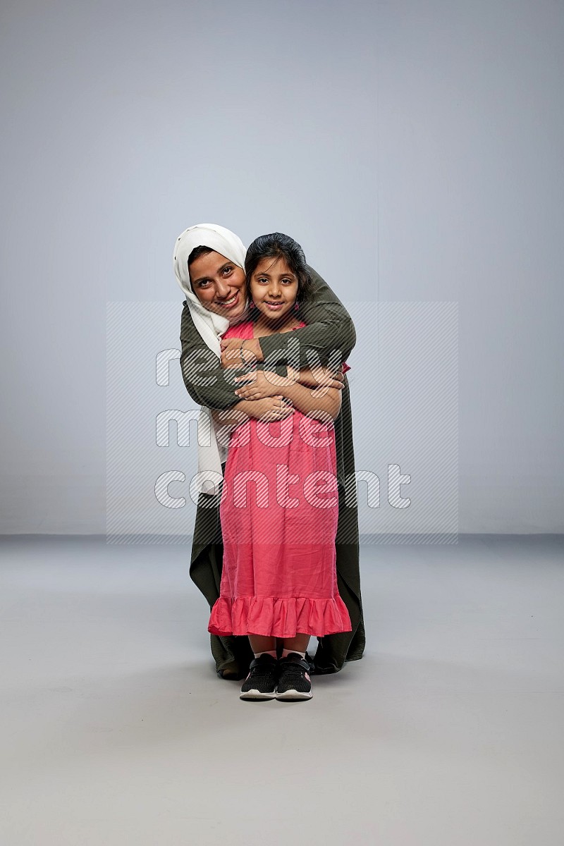 A girl and her mother interacting with the camera on gray background