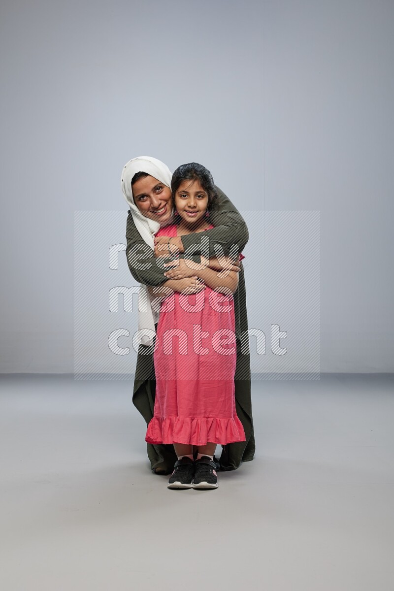 A girl and her mother interacting with the camera on gray background