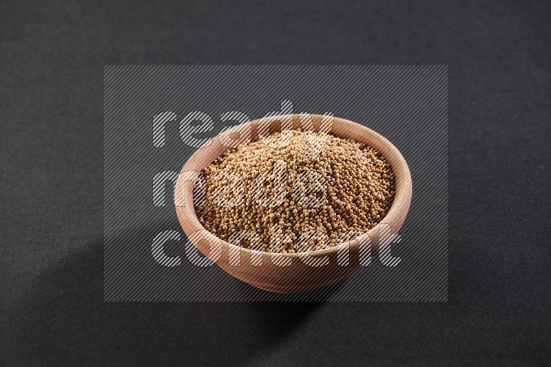 A wooden bowl full of mustard seeds on a black flooring in different angles