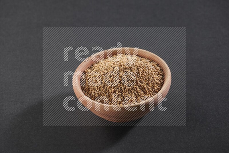 A wooden bowl full of mustard seeds on a black flooring