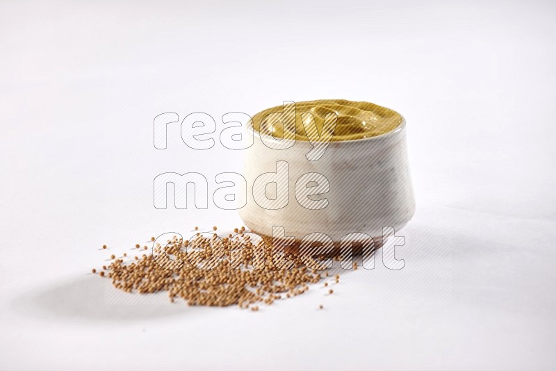 A beige pottery bowl full of mustard paste with mustard seeds underneath on white flooring in different angles