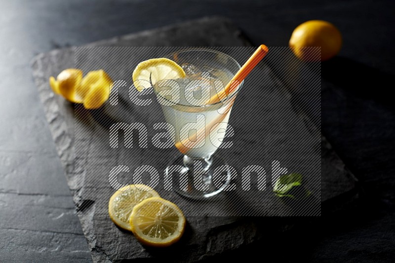 A glass of lemon juice with a straw on black background