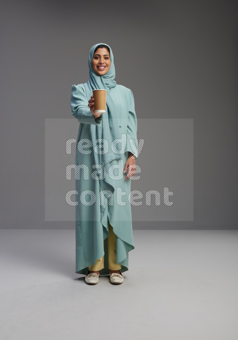 Saudi Woman wearing Abaya standing  holding paper cup on Gray background