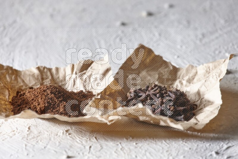 Cloves powder and cloves on 2 crumpled pieces of paper on a textured white flooring