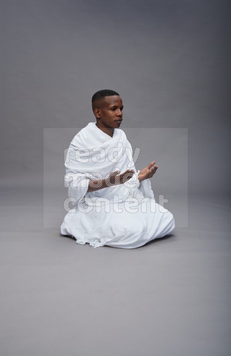 A man wearing Ehram sitting on floor dua'a on gray background