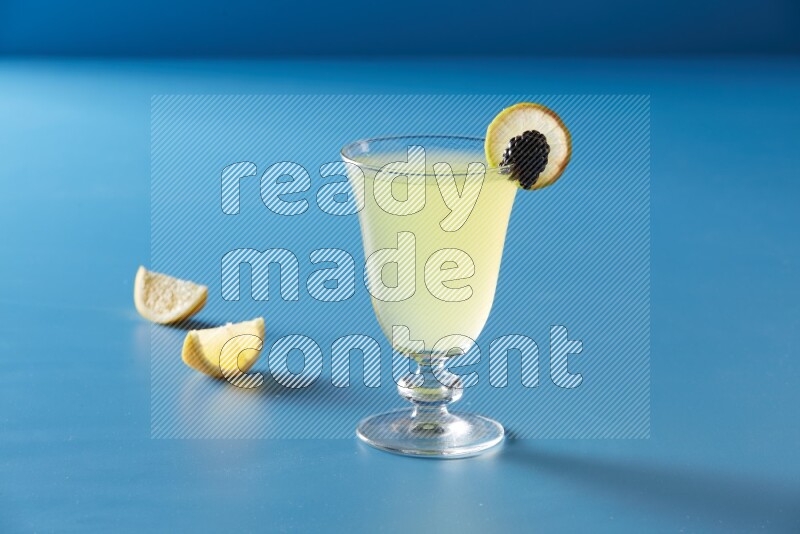 glass of lemon juice with lemon slice and berry on blue background
