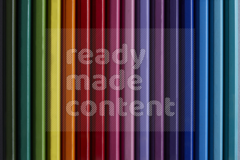 مجموعة من أقلام الرصاص الملونة مرتبة لتعرض تدرجا من الألوان المختلفة علي خلفية رمادية