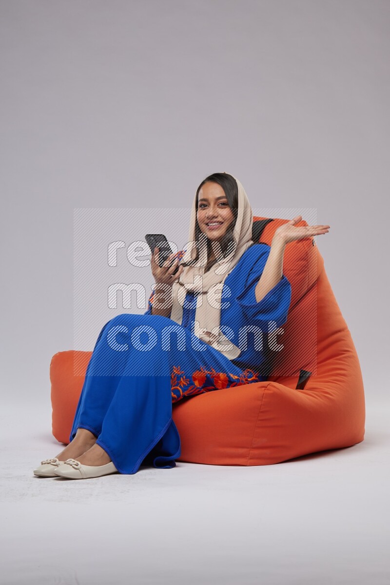 A Saudi woman sitting on an orange beanbag and texting on phone