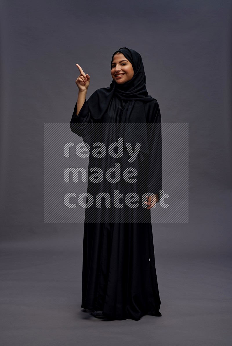 Saudi woman wearing Abaya standing interacting with the camera on gray background