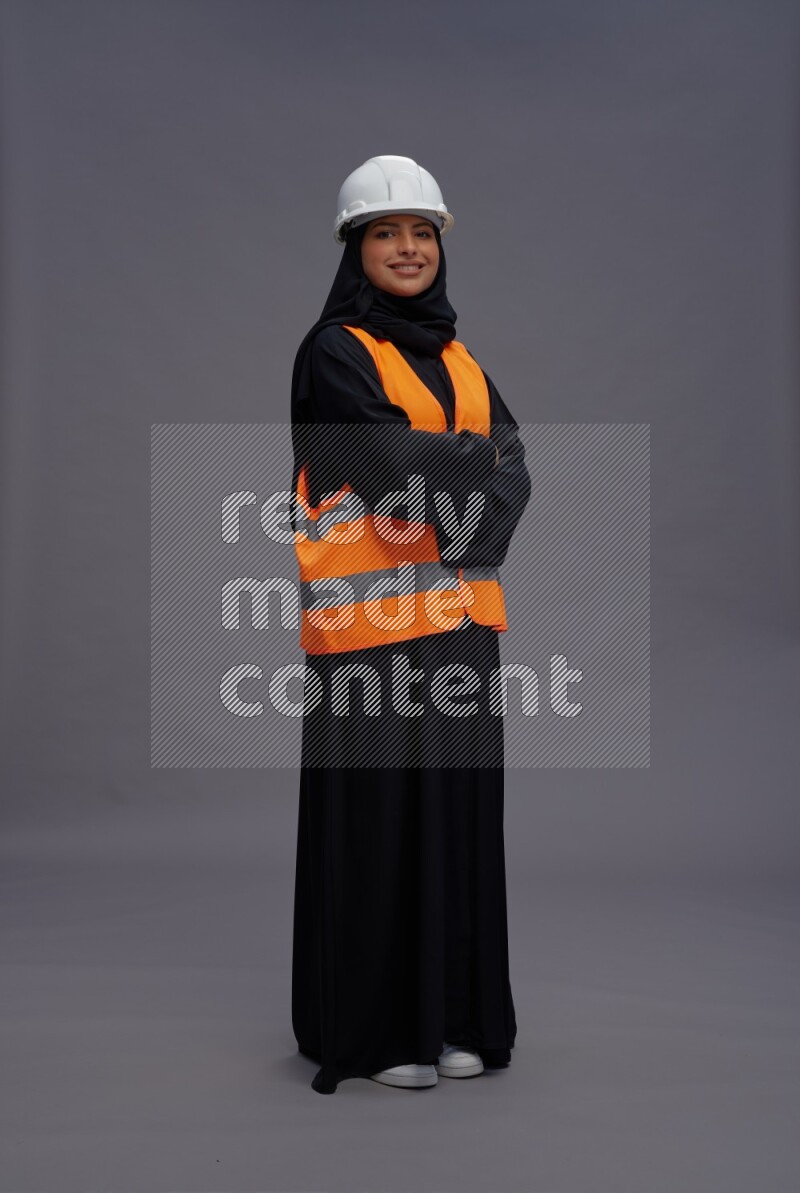 Saudi woman wearing Abaya with engineer vest standing with crossed arms on gray background