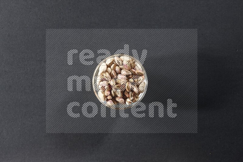 A glass bowl full of peeled pistachios on a black background in different angles