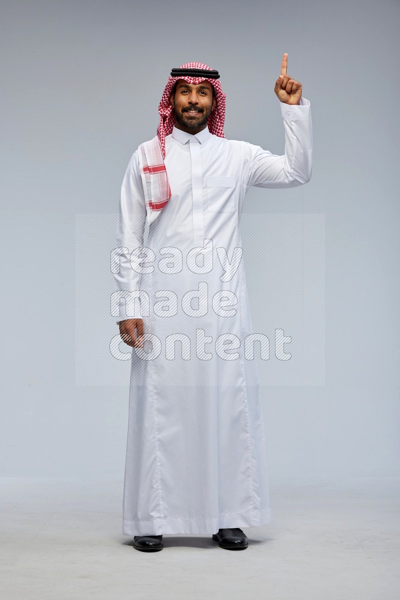 Saudi man Wearing Thob and shomag standing interacting with the camera on Gray background