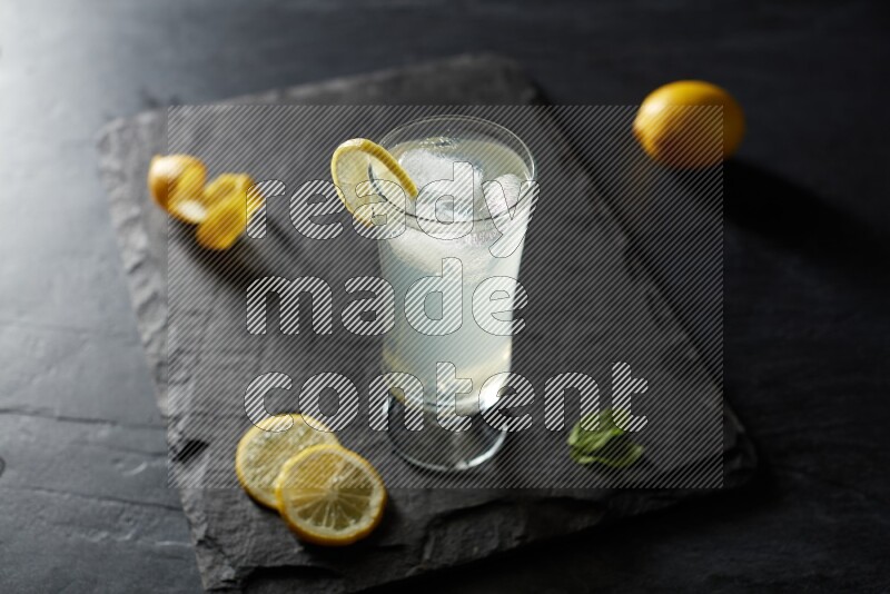 A glass of lemon juice with a lemon slice on black background