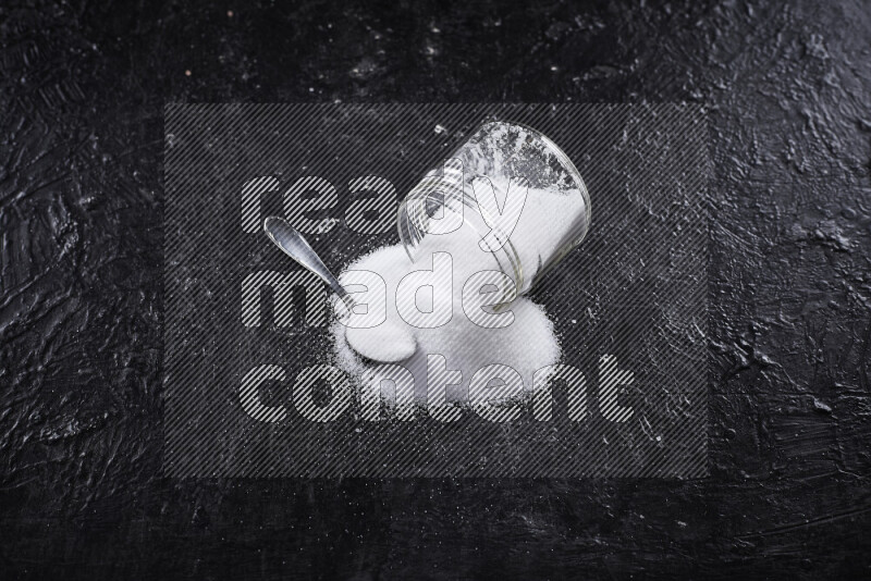 A glass jar full of fine table salt on black background