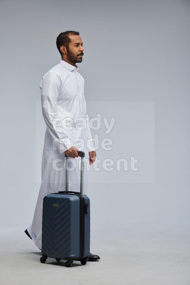 Saudi man wearing thob standing holding Travel bag on Gray background