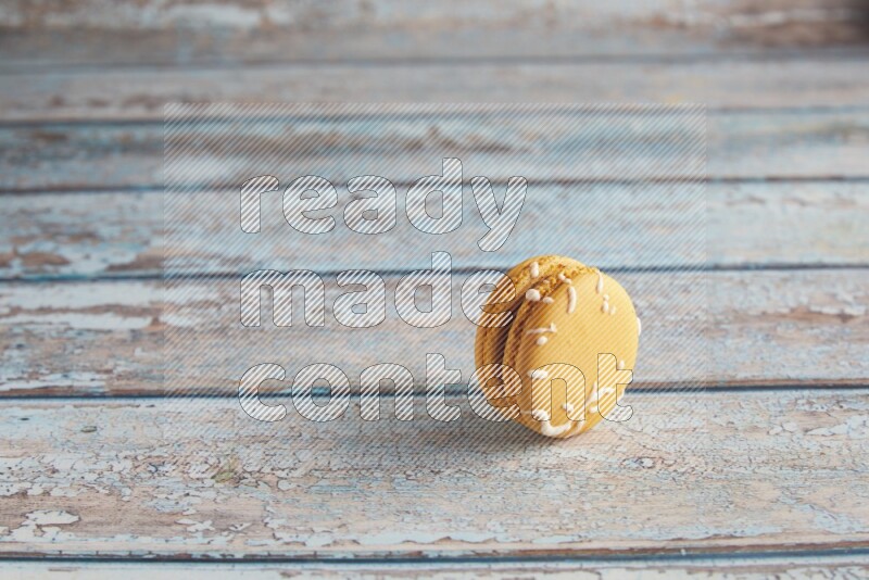 45º Shot of Yellow Piña Colada macaron on light blue wooden background
