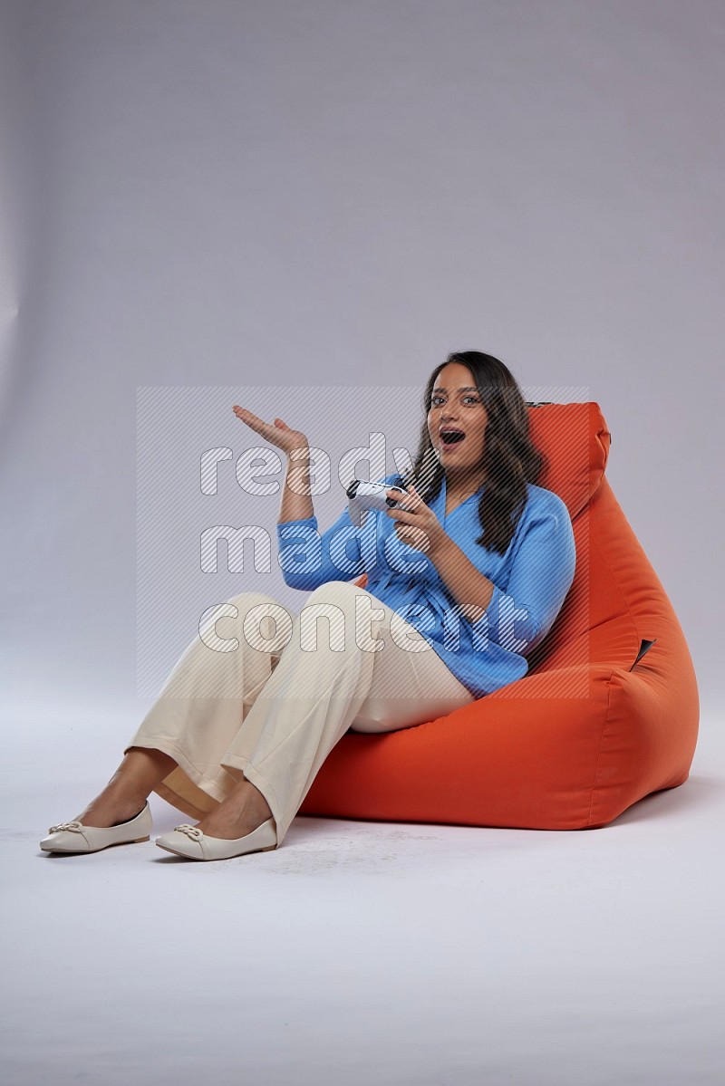 A woman sitting on an orange beanbag and gaming with joystick