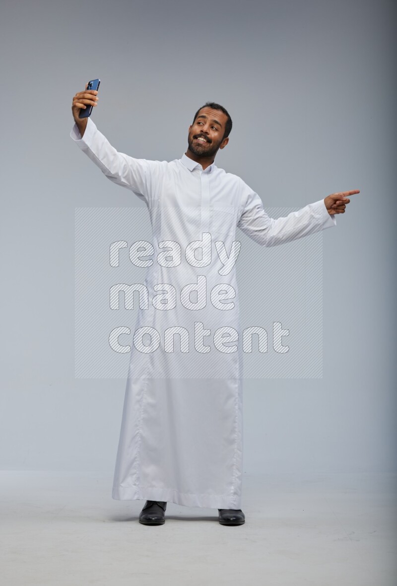Saudi man wearing Thob standing taking selfie on Gray background