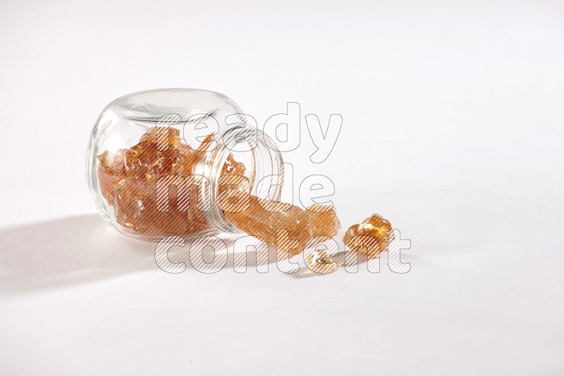 A glass spice jar full of gum arabic and jar is flipped with fallen pieces on white flooring