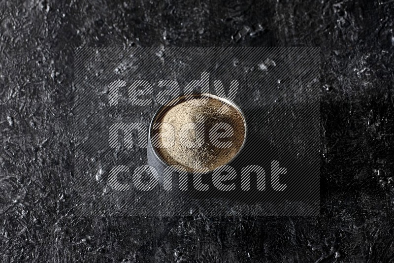 Black pottery bowl full of white pepper powder on textured black flooring