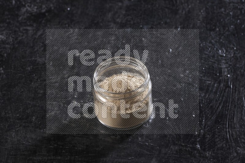 A glass jar full of garlic powder on a textured black flooring