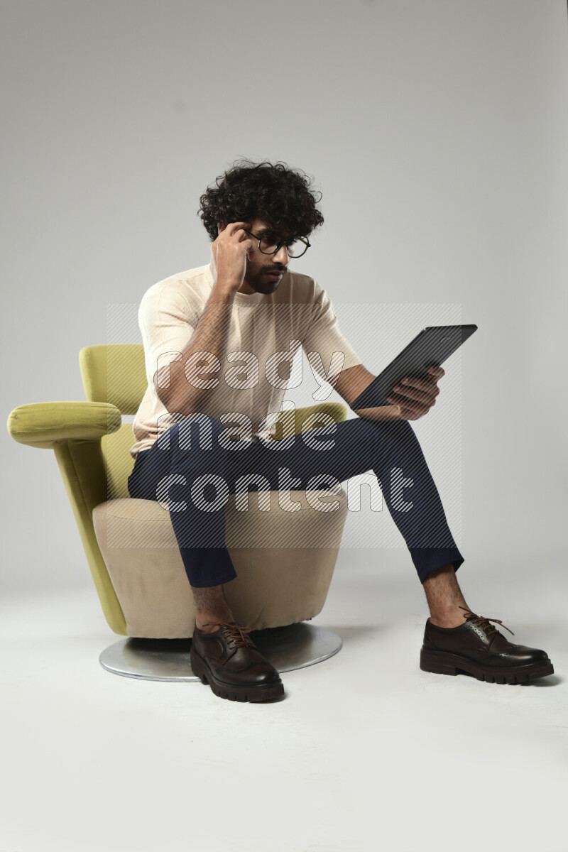 A man wearing casual sitting on a chair browsing on a tablet on white background