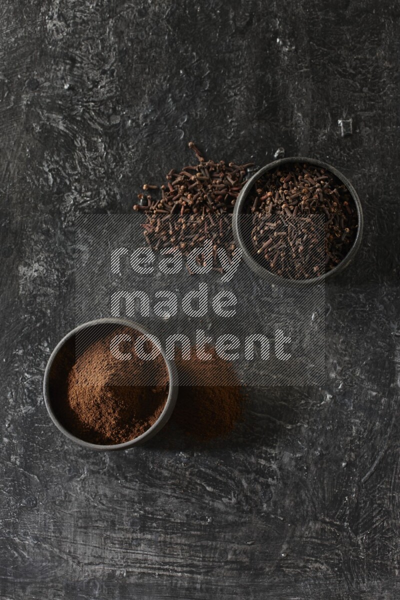 وعاءين من الفخار الأسود أحدهما ممتلئي بحبوب القرنفل والآخر ممتلئ ببودرة القرنفل على خلفية سوداء