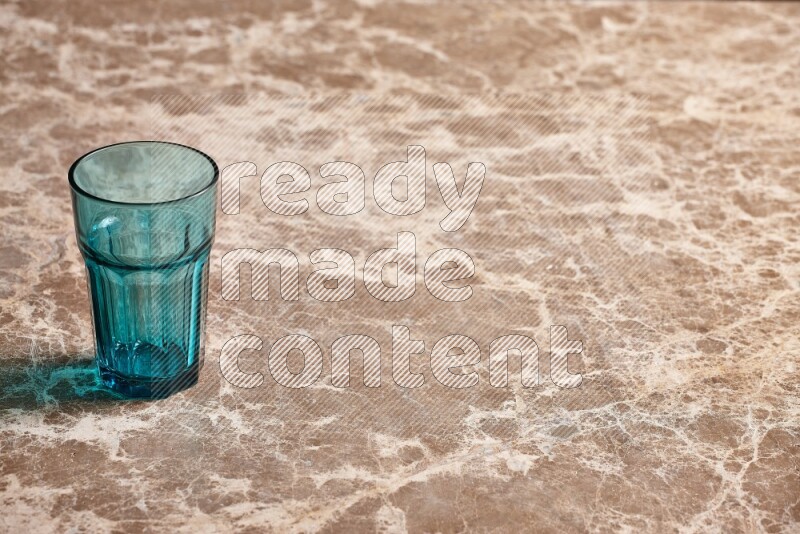 A turquoise glass cup on beige marble background