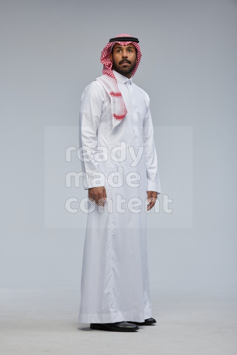 Saudi man Wearing Thob and shomag standing interacting with the camera on Gray background