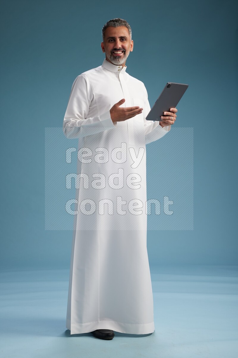 Saudi man waring thob with tablet on blue background