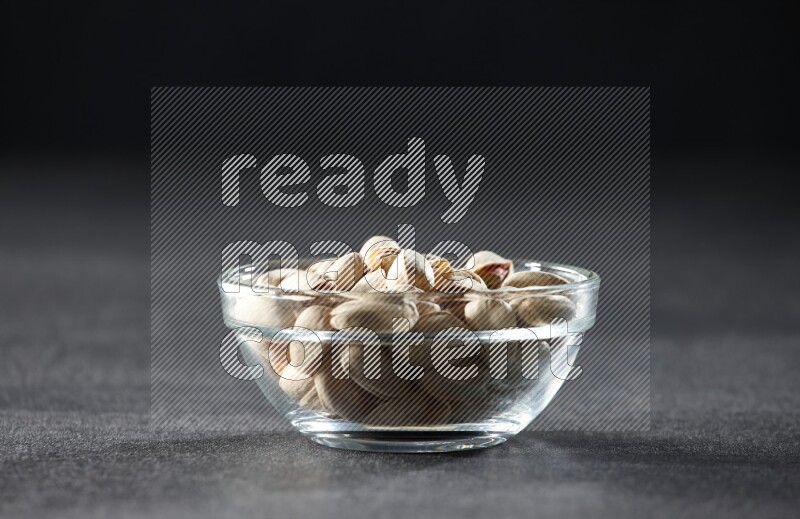 A glass bowl full of pistachios on a black background in different angles