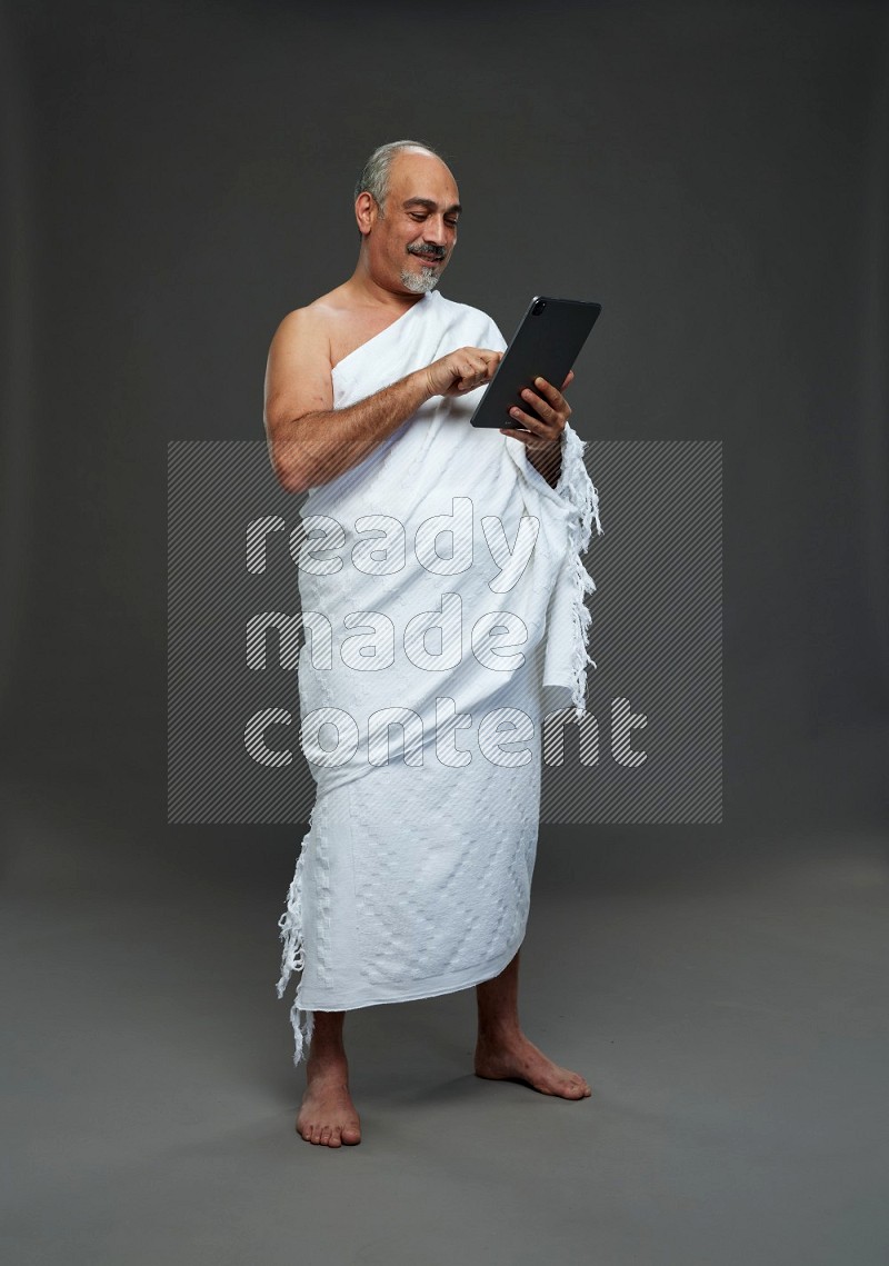 A man wearing Ehram Standing working on tablet on gray background