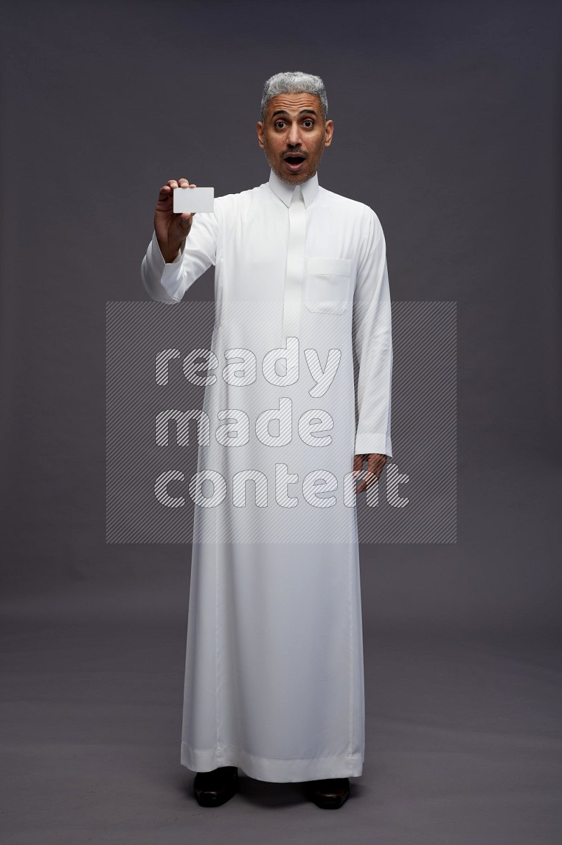 Saudi man wearing thob standing holding ATM card on gray background