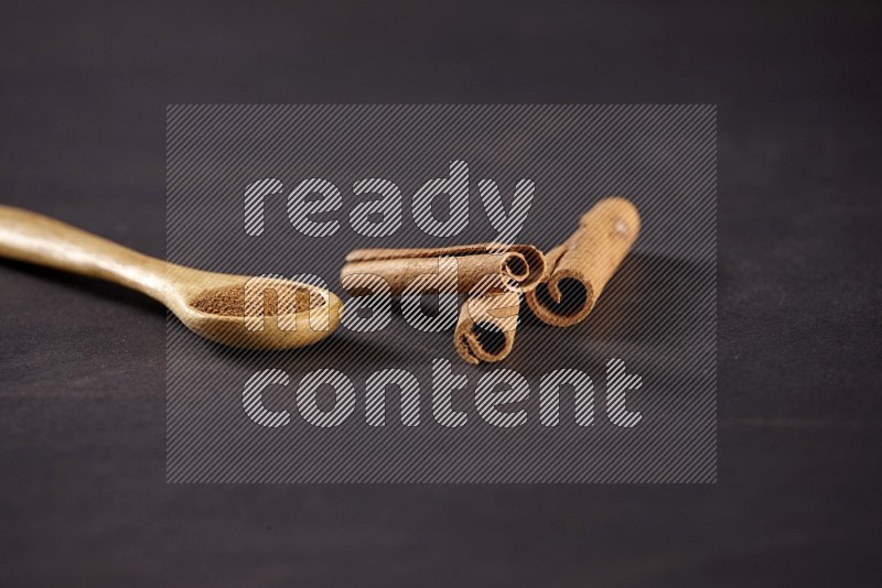 3 Cinnamon sticks stacked beside a wooden spoon full of cinnamon powder on black background in different angles