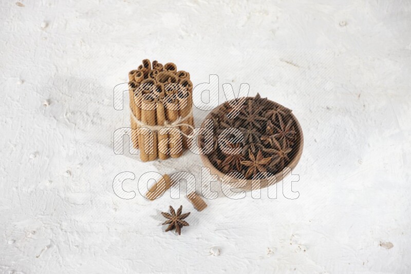 A stacked and bounded cinnamon sticks and a wooden bowl full of star anise on a white background