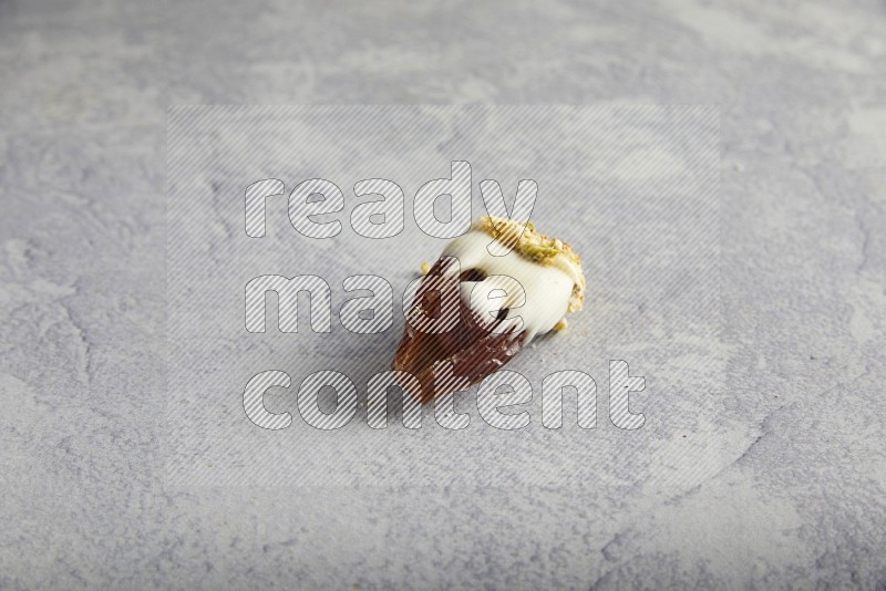 Hazulnut stuffed date covered with white chocolate and crushed peanuts & pistachios on light grey background
