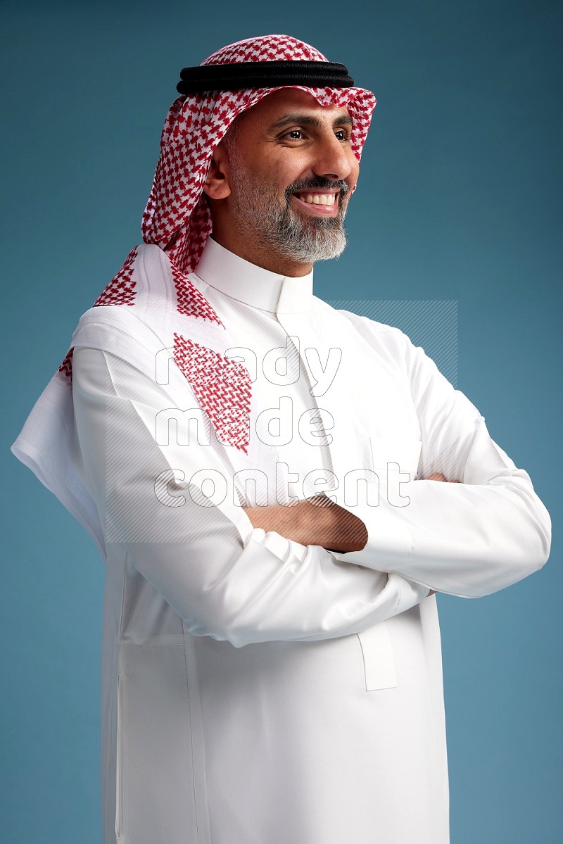 Saudi man wearing thob and shomagh posing to the camera on blue background