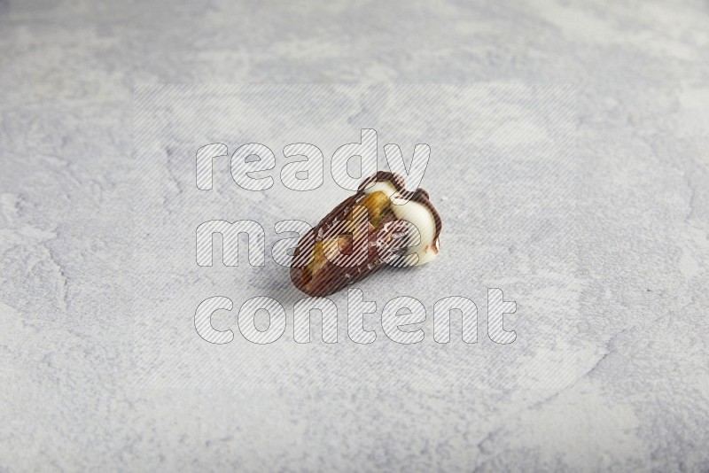 pistachio stuffed date covered with white chocolate with dark chocolate drizzle on a light grey background