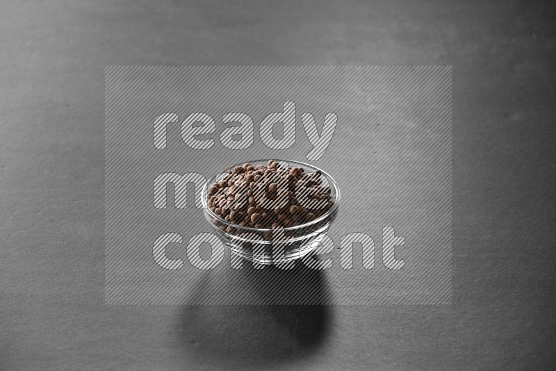 A glass bowl full of allspice on black flooring