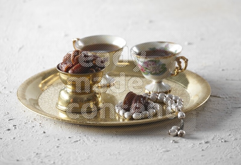 Dates in a metal bowl with tea and prayer beads on a tray in a light setup